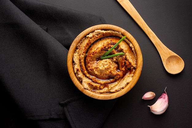 Foto gratuita fotografía cenital de hummus en un cuenco de madera con una cuchara de madera y trozos de ajo en el cuadro negro