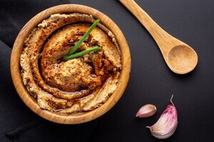 Foto gratuita fotografía cenital de hummus en un cuenco de madera con una cuchara de madera y trozos de ajo en el cuadro negro