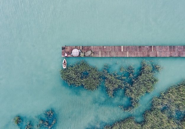 Fotografía cenital de un muelle de madera en la costa con un barco de pesca al lado