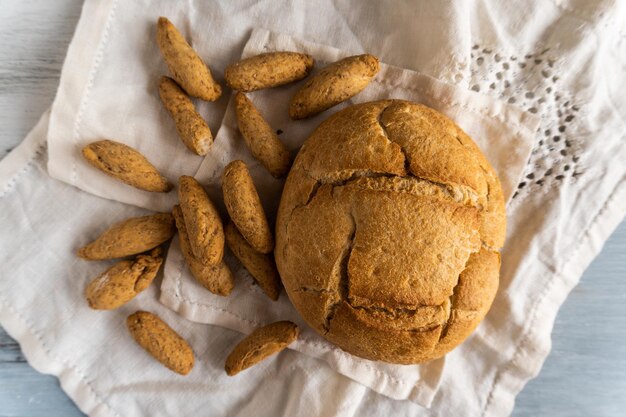 Fotografía cenital de un pan redondo tradicional casero y palitos de pan sobre una mesa rústica de madera