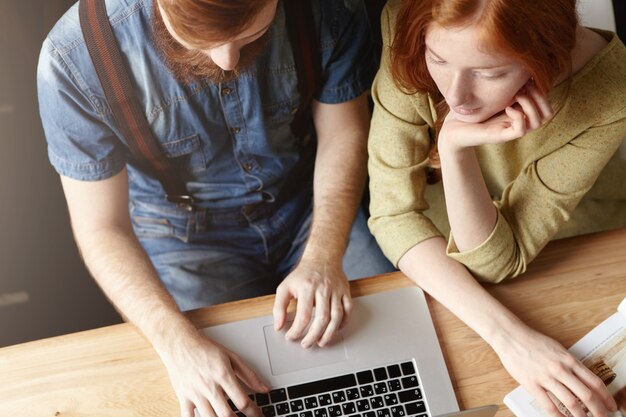 Fotografía cenital de pareja usando laptop sentado en casa o café.