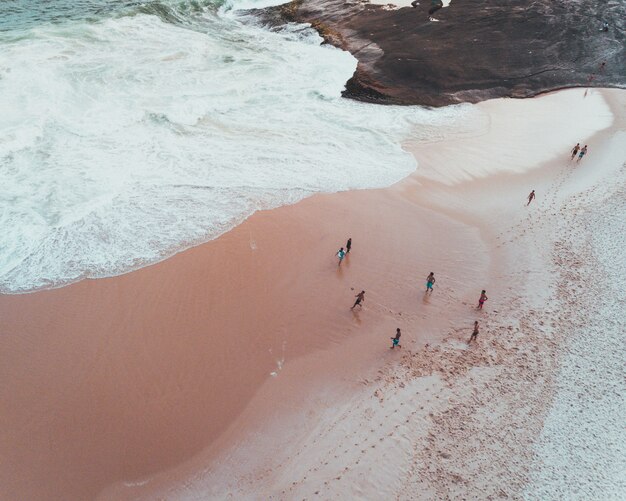 Fotografía cenital de personas disfrutando de un día soleado en una playa de arena cerca de hermosas olas del mar