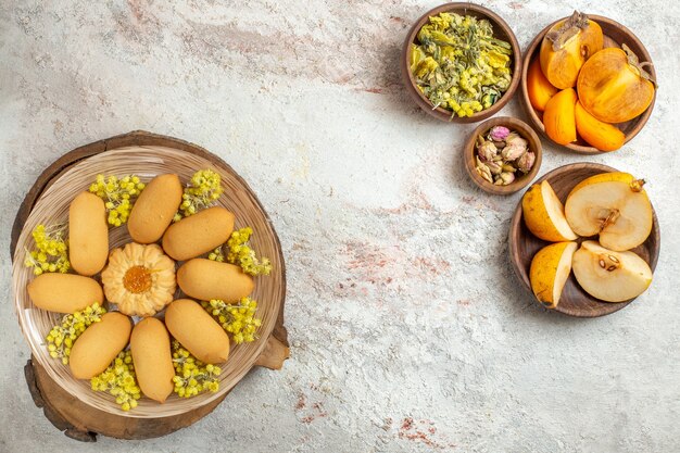 Fotografía cenital de un plato de galletas y tazones de frutas y flores secas sobre suelo de mármol