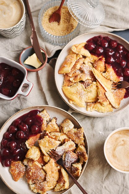 Fotografía cenital vertical de deliciosos panqueques esponjosos con cereza y azúcar en polvo