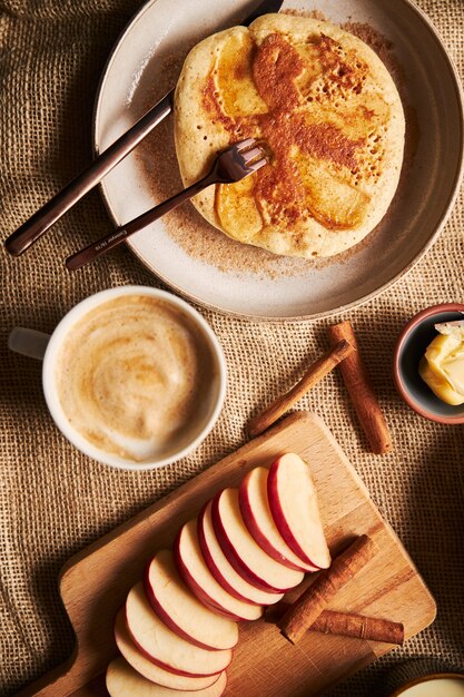 Fotografía cenital vertical de tortitas de manzana con manzanas, café, canela y mantequilla en el lateral