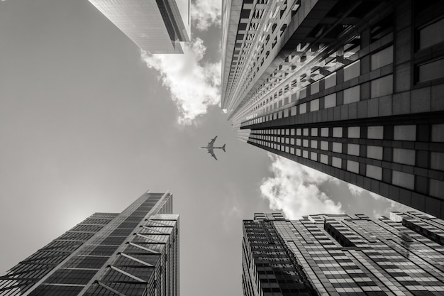 Fotografía en escala de gris de bajo ángulo de un avión volando sobre edificios de gran altura