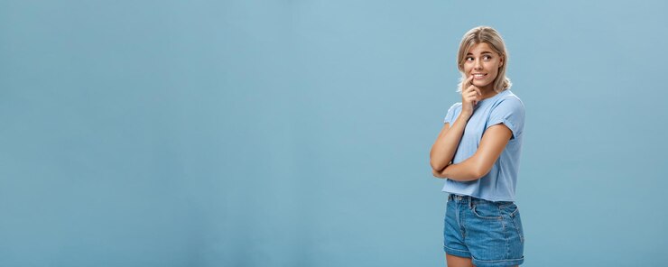 Foto gratuito fotografía interior de femenina romántica y tímida mujer europea de buen aspecto con cabello blanco sosteniendo el dedo en el labio sonriendo curiosa e intrigada mientras gira a la derecha y observa algo interesante