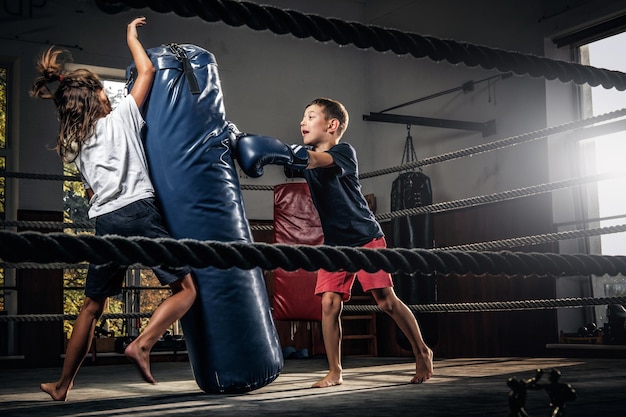 Fotografía oscura de niños entrenando con un gran saco de boxeo en el estudio de boxeo.