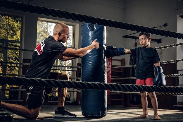 Fotografía oscura de niños entrenando con un gran saco de boxeo en el estudio de boxeo.