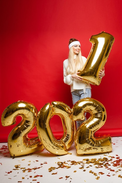 Fotografía de Stock de atractiva chica rubia con sombrero de Santa, suéter y jeans sosteniendo el dígito uno en las manos.