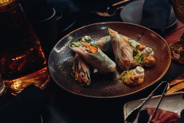 Fotografía de Stock de comida contemporánea servida en plato de moda en restaurante. Rollos de verduras saludables con salsas servidas en un plato.