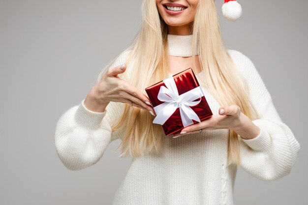 Foto gratuita fotografía de stock de irreconocible mujer rubia sonriente con cabello largo sosteniendo un pequeño regalo de navidad envuelto en papel de regalo rojo y lazo blanco.