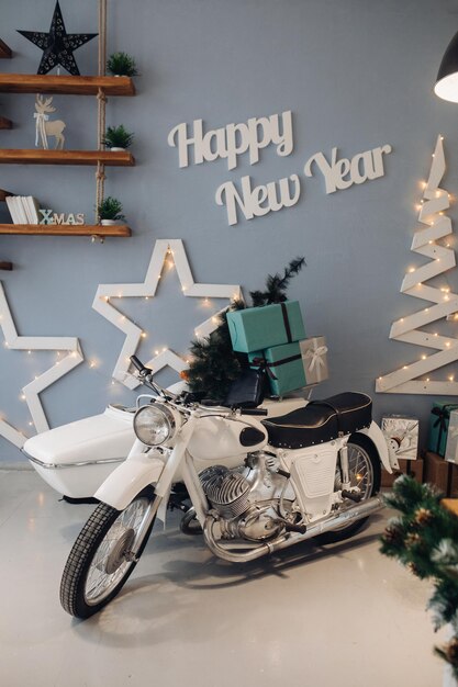 Fotografía de Stock de motocicleta blanca con minuature árbol de Navidad y regalos de Navidad envueltos en la cuna. Interior atmosférico para el día de Navidad. 2020 año nuevo.