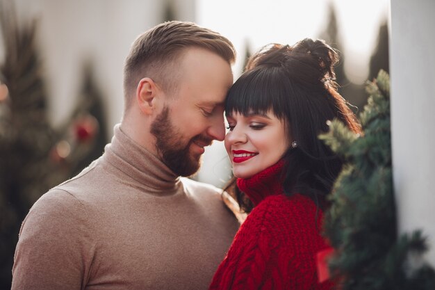 Fotografía de Stock de pareja cariñosa rodeada de abetos. Hombre mirando a su encantadora esposa.