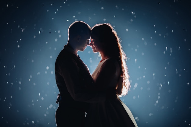 Fotografía de Stock de una romántica pareja de recién casados abrazándose cara a cara contra el fondo oscuro iluminado con destellos brillantes alrededor.