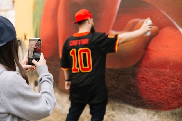 Fotografía de toma de mujer de hombre rociando en la pared de graffiti