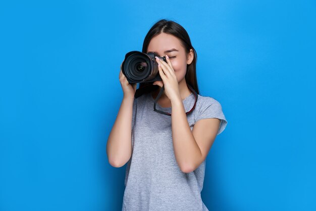 Fotógrafo asiático hermoso joven enfocado por la cámara réflex digital profesional y en la pared azul