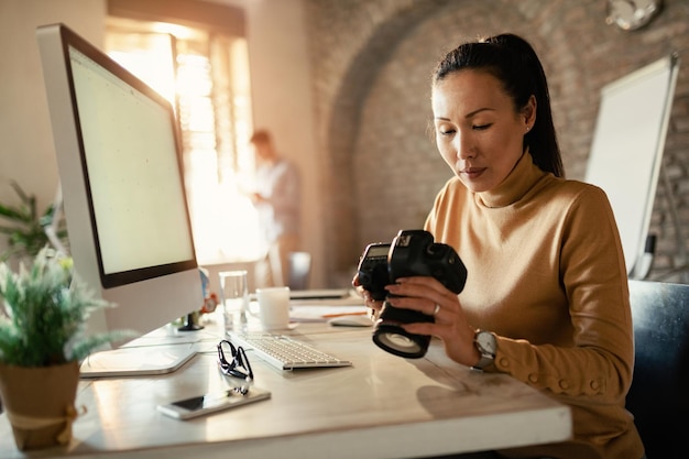 Fotógrafo asiático mirando imágenes en una cámara digital mientras trabaja en su oficina