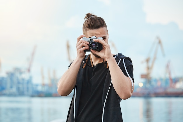 Fotógrafo con cámara vintage tomando fotos cerca del mar, caminando por la ciudad para fotografiar cada momento interesante