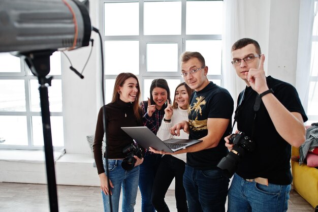 Fotógrafo explicando sobre la toma a su equipo en el estudio y mirando en la computadora portátil Hablando con sus asistentes sosteniendo una cámara durante una sesión de fotos Trabajo en equipo y lluvia de ideas