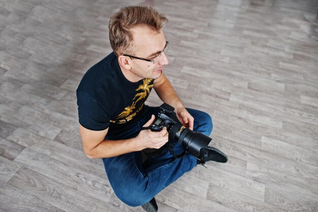 Fotógrafo de hombre sentado en el suelo en el estudio Fotógrafo profesional en el trabajo