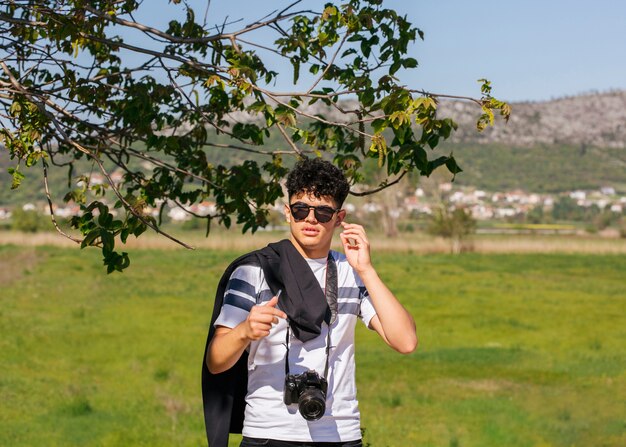 Fotógrafo joven con la cámara que se coloca en paisaje verde