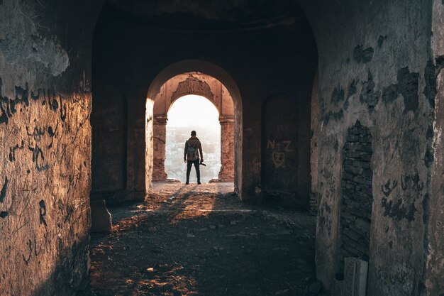 Fotógrafo masculino de pie en el arco de una vieja arquitectura abandonada