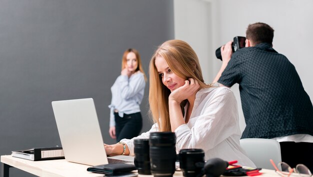 Fotógrafo con modelo en el fondo y mujer que trabaja en la computadora portátil