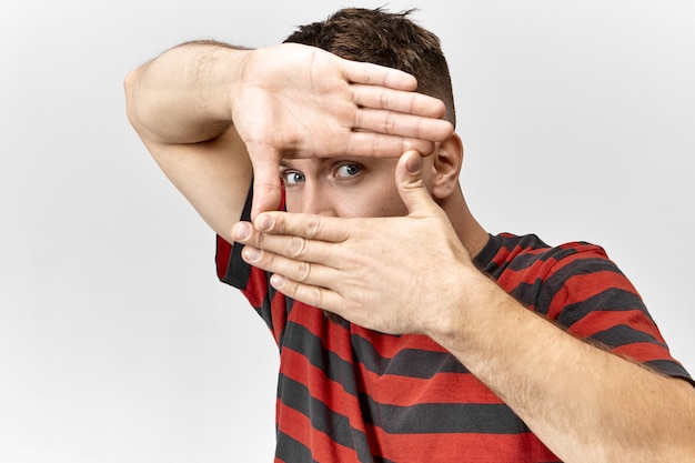 Fotógrafo de ojos azules guapo vestido con camiseta elegante haciendo marco de fotos con sus manos, centrándose en los ojos, enseñando a los estudiantes a tomar fotografías. Gente, estilo de vida, diversión y lenguaje corporal