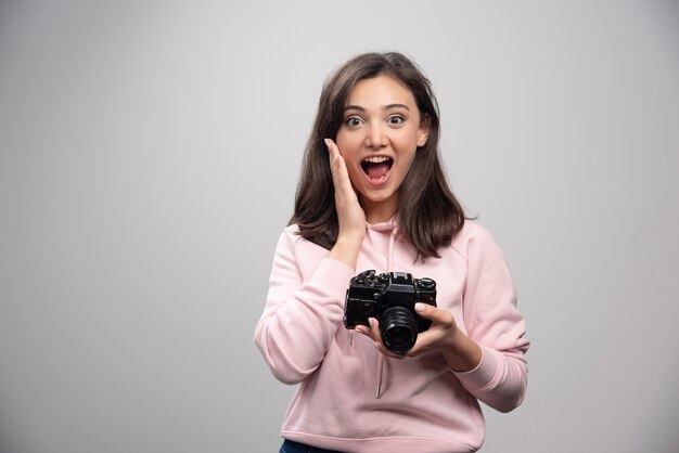 Fotógrafo de sexo femenino que presenta con la cámara en la pared gris.