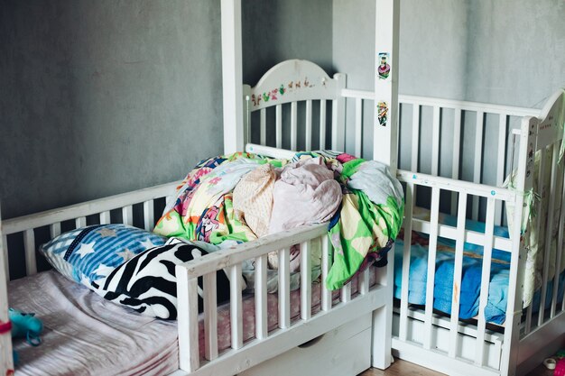 Fragmento de una foto de la habitación de un niño con cosas esparcidas, almohadas y colchas en las camas