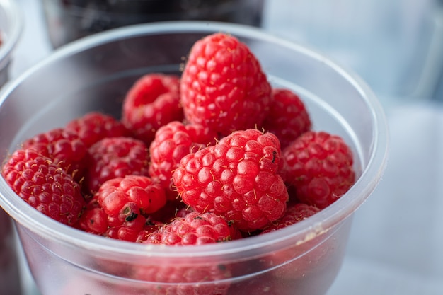 Frambuesas dulces, sabrosas, rojas y frescas en una pequeña taza de plástico