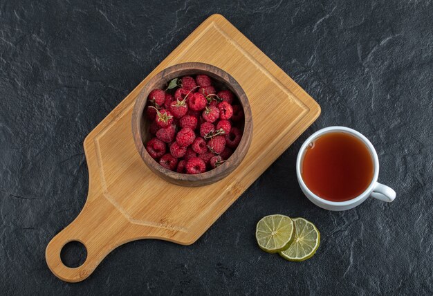 Frambuesas frescas sobre tabla de madera con té y limón.