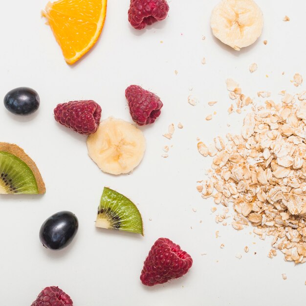 Frambuesas; uvas; plátano; Rodajas de kiwi y naranja con lagos de avena sobre fondo blanco