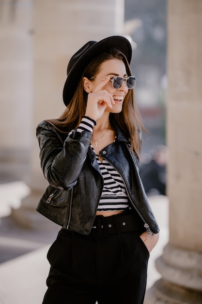 Francés joven de pelo castaño con una chaqueta de cuero, sombrero negro en el paseo de la ciudad