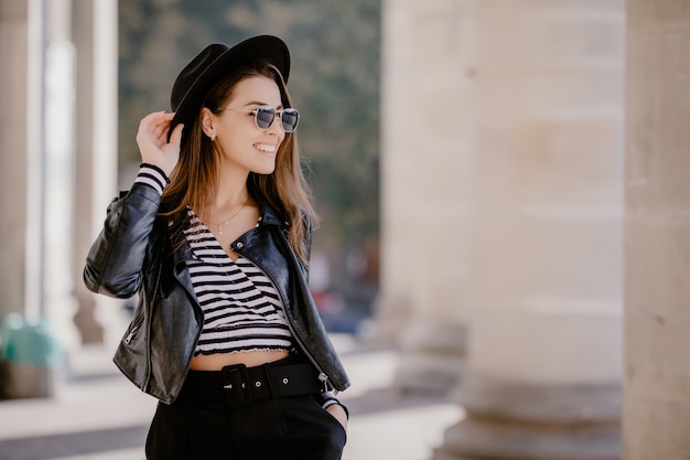 Foto gratuita francés joven de pelo castaño con una chaqueta de cuero, sombrero negro en el paseo de la ciudad
