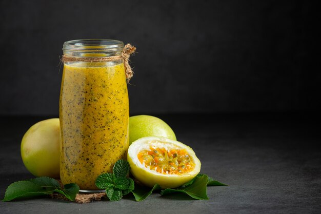 un frasco de jugo de maracuyá y fruta de la pasión fresca cortada por la mitad en un piso oscuro