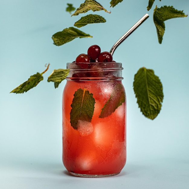 Foto gratuita frasco de vidrio de bebidas con tarta de cerezas y hojas de menta aislado sobre fondo azul.