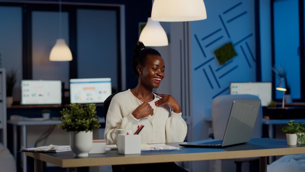 Freelancer africano feliz recibiendo buenas noticias en la computadora portátil trabajando horas extras en la oficina de la empresa de puesta en marcha