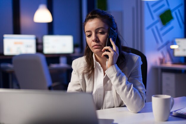 Freelancer corporativo cansado que tiene una conversación por teléfono mientras trabaja agotado para las estadísticas económicas