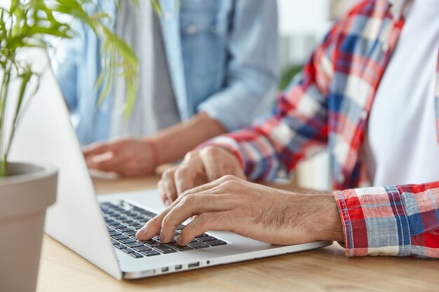 Freelancer hombre irreconocible y su socio teclados en la computadora portátil, trabajan a distancia