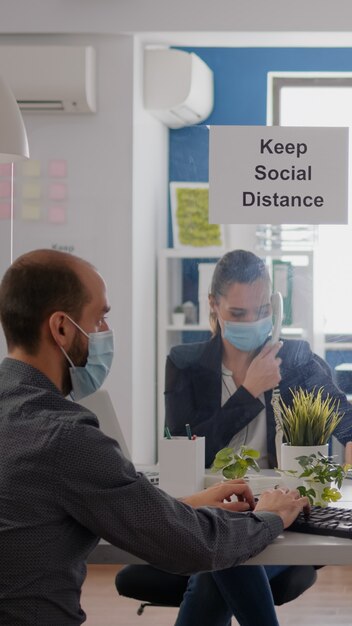 Freelancer con mascarilla médica de protección que trabaja en una computadora portátil mientras habla por teléfono con el equipo