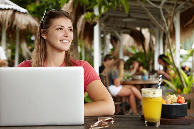 Freelancer mujer caucásica con peinado largo que trabaja de forma remota en una computadora portátil moderna, usando wi-fi gratis durante el desayuno en el café