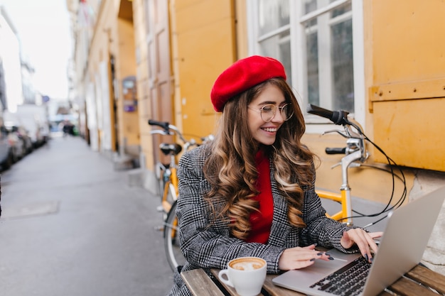 Freelancer mujer sonriente ocupado pasar tiempo en la cafetería al aire libre