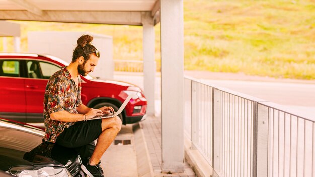 Freelancer sentado en el capó y trabajando de forma remota