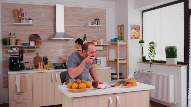 Freelancer tomando café y trabajando en la computadora portátil durante el desayuno en la cocina. Emprendedor en pijama trabajando en una computadora portátil desde casa en la cocina.