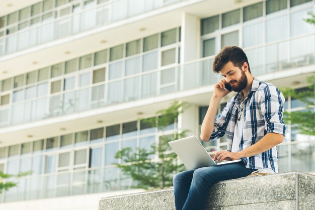 Freelancer usando laptop y teléfono al aire libre en verano