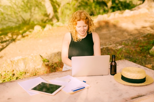 Foto gratuita freelancing femenino joven en el ordenador portátil en el escritorio en naturaleza