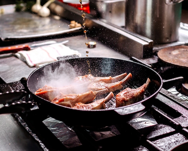 Freír carne de costillas dentro de una sartén negra en la cocina