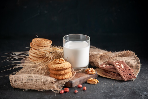 Frente a la vista cercana de una leche fresca en un vaso de galletas picos en una toalla de color nude nueces cacahuetes sobre fondo de onda negra